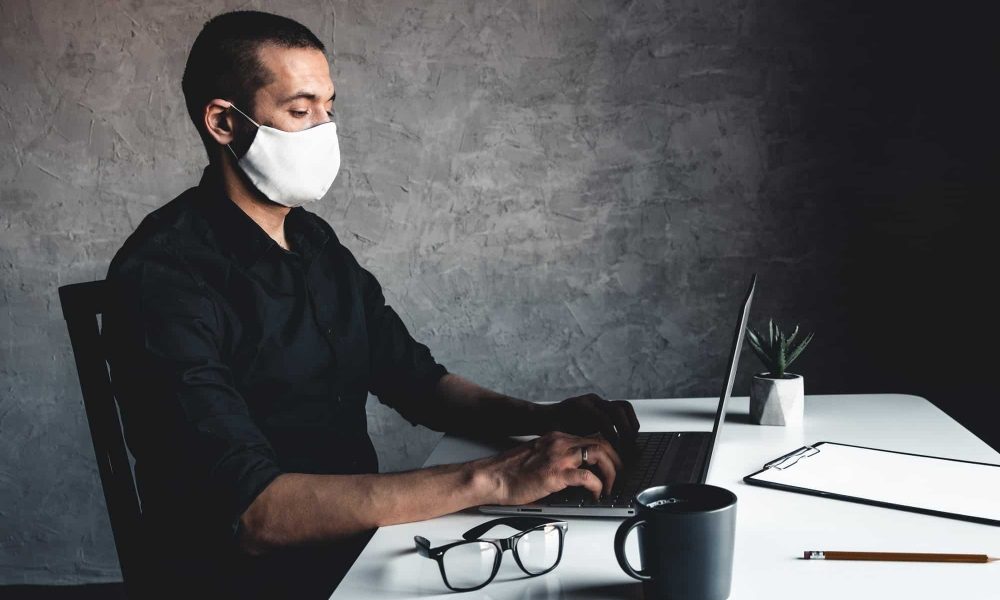 A masked man works at a computer. Pandemic, coronavirus, epidemic